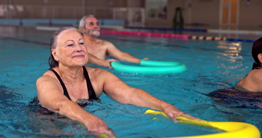 Senior woman exercising with pool noodle during water aerobics class | Shutterstock HD Video #1065105523