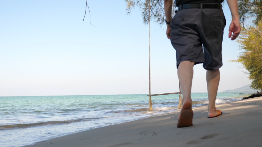 Trat Beach Sea Sand Thailand. An Asian man walking on a beach towards a swing hanging from the tree near the seashore. Summer vacations.
