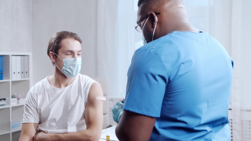 African-American doctor makes a coronavirus vaccine using a syringe and hypodermic needle. Medical worker and patient at the hospital office. Vaccination and safety concept. | Shutterstock HD Video #1065108802