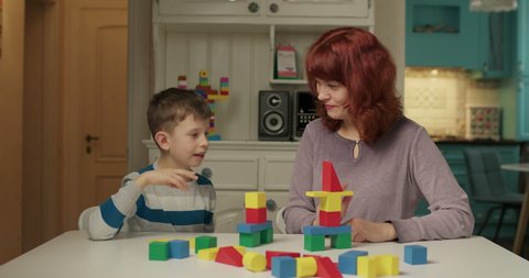 Autism psychologist working with child with autism with color wooden blocks. School boy with autism learning with mother at home. Kid building with wood blocks. Autism education.