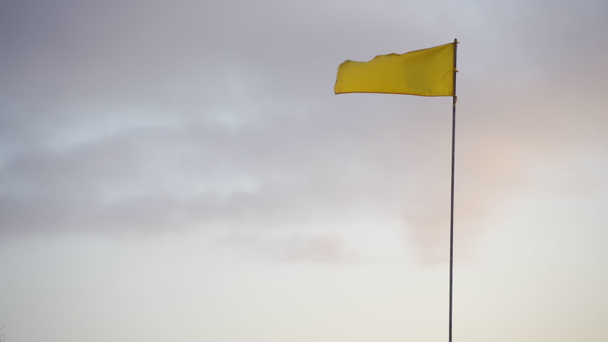 Lockdown Low Angle Wide View Of Yellow Flag In Wind At Sunrise Against Cloudy Sky, Tanah Lot, Bali, Indonesia