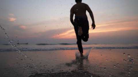 A young man splashes the water while sprinting or running  towards the sea during sunrise. Healthy lifestyle, Motivational or inspiration concept