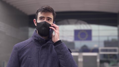 Man with face mask on a phone call in front of European Parliament in Brussels. Concerned EU Politician or Businessman in times of Coronavirus Crisis in Europe