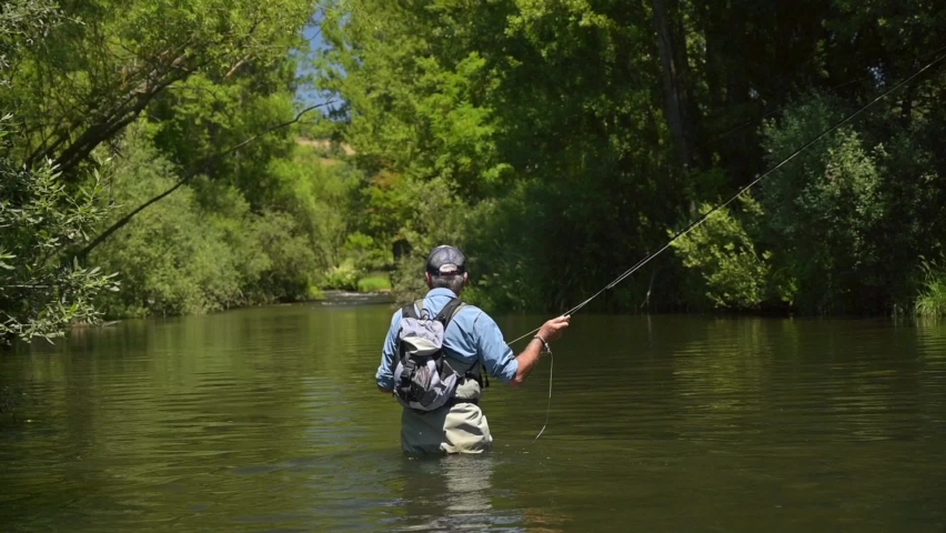 fly fisherman in summer fishing in a mountain river with waders and a cap