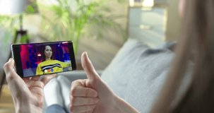 Girl having video conference on smartphone with Caucasian female friend while resting on couch in room. Woman talking in online chat with joyful girl and waving her hand. Conversation concept