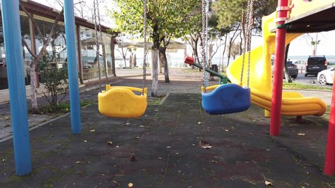 Turkey, Istanbul, January 2020. Summer sunny day. Bright sunlight. Nobody. No people. Empty playground in city park on embankment. metal swing swinging in wind. Green leaves on trees.