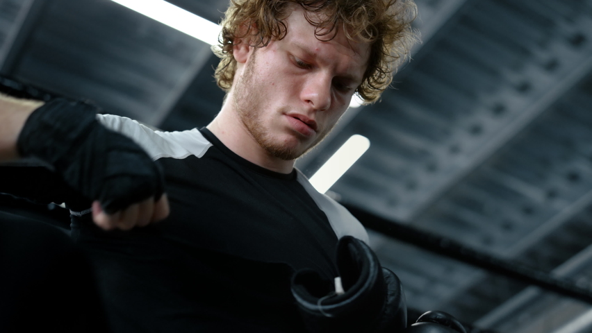 Portrait of focused kickboxer putting on boxing gloves at gym. Closeup strict sportsman ending preparation for fight in sport club. Aggressive fighter hitting hands in fitness center. Royalty-Free Stock Footage #1065132901