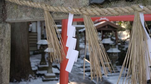 Shide hung from the torii gate of a shrine. Shide is strips of paper cut and folded in a specific way that are attached to and suspended from a sacred straw rope. Snow temple background