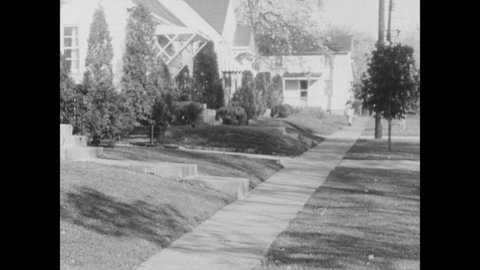 1960s: Boy walks down sidewalk, throws newspapers on to doorsteps.