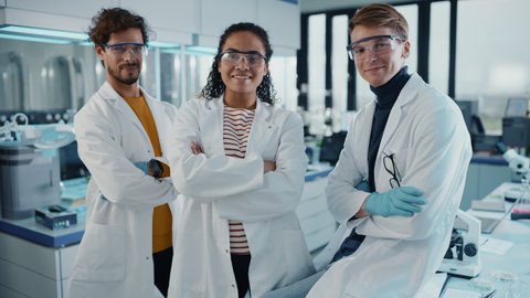 Medical Science Laboratory with Team of Three Young Successful Scientists. Beautiful Black Female, Handsome Latin and Caucasian Male Scientists Smile while Looking at Camera. Medium Portrait Pose Shot