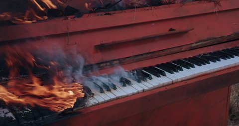 Close up pano of burning orange piano in a autumn field during a snowfall. Flames and smoke around. The art concept scene.