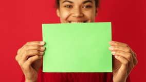 Attention. Close up of smiling mixed race woman showing empty blank paper sign board with copy space for text or design isolated over red background. Green screen. Selective focus - Powered by Shutterstock - Get 15% off with code: PIKWIZARD15