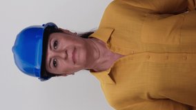 An elderly female civil engineer wearing a blue hard hat is smiling at the camera on a white background.Video for the vertical story.