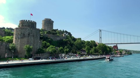 Footage of a yacht passing on Bosphorus strait and people walking at upscale neighborhood called "Rumeli Hisari". Historical fortress and FSM bridge are in the view. It is a beautiful Istanbul scene.
