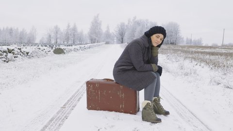 Stressful woman hitchhiker sitting on vintage suitcase