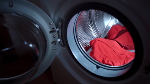 Housewife preparing dirty laundry with stains for washing, woman's hand throwing two liquid concentrated capsules of washing detergent into the spinning cylinder and closing washing machine door