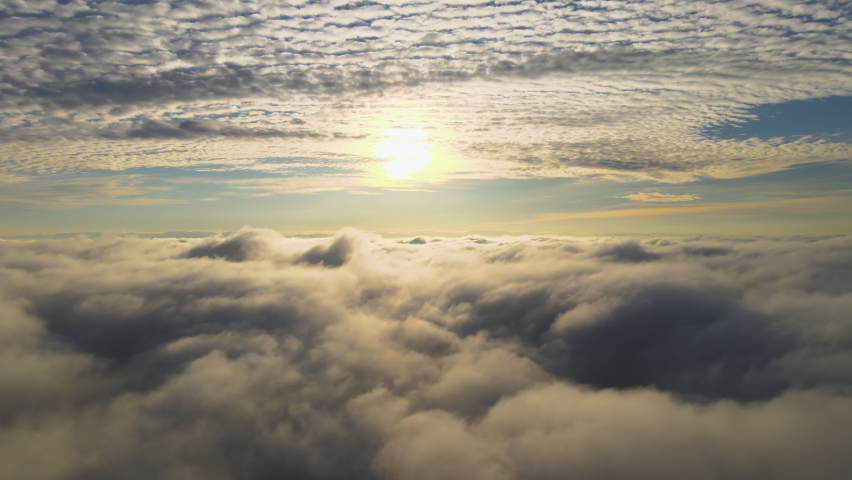 Aerial view of vibrant yellow sunrise over white dense clouds with blue sky overhead. | Shutterstock HD Video #1065158974
