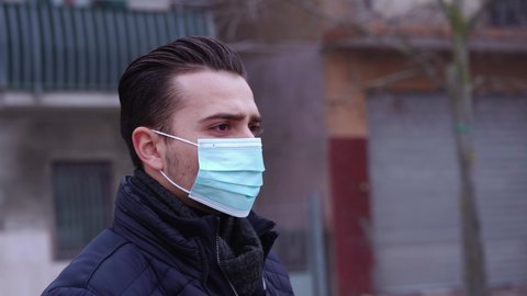 Serious man puts on blue medical mask among rotating city