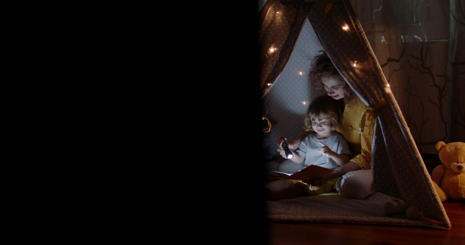 Happy caucasian mom and her cute baby boy spending time together at home, reading a book, using a flashlight in a cozy tent - happy family 4k footage Royalty-Free Stock Footage #1065164929