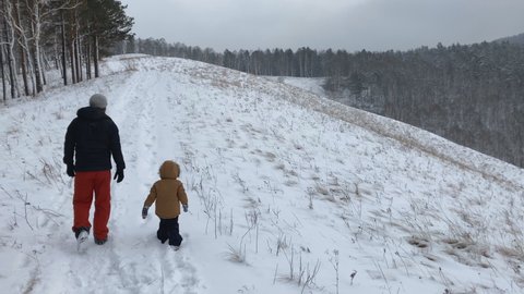A father and his young son walk in the mountains in winter.