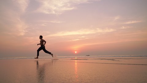 A young man running or sprinting on the beach against the rising sun. Healthy lifestyle. Motivational or inspiration concept