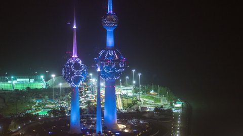 KUWAIT - CIRCA FEB 2019: Top view of Kuwait Towers night timelapse illuminated at night - the best known landmark of Kuwait City. Kuwait, Middle East. View with park with attractions at foggy weather.