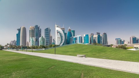The high-rise district of Doha timelapse hyperlapse, seen from the Hotel Park, with green lawn and artificial hill in the foreground. Skyscrapers and palms