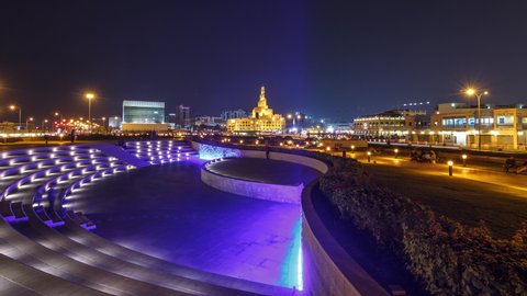 Small amphitheatre in Souq Waqif Park at night timelapse hyperlapse in Doha, with vegetation and buildings in the distance, including illuminated islamic center.