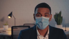 african american businessman in medical mask looking at camera in office