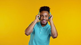Handsome african man having fun, dancing with blue headphones in yellow studio. Music, dance, radio concept, slow motion
