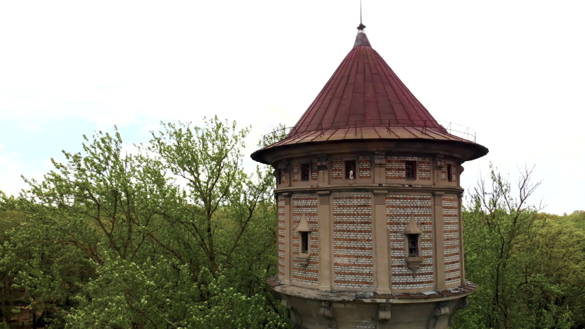 Aerial flight out: Scenic old water tower surrounded by green trees during daytime