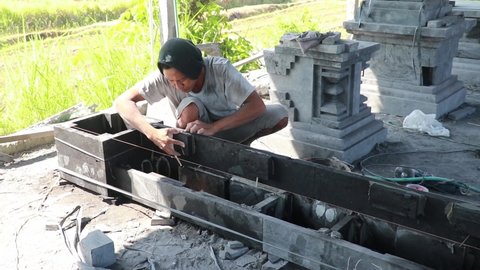 A stonemason makes an altar to a Hindu temple on the island of Bali in Indonesia. A man joins and glues stone slabs. Man Chiseling Stone with Hand Tools