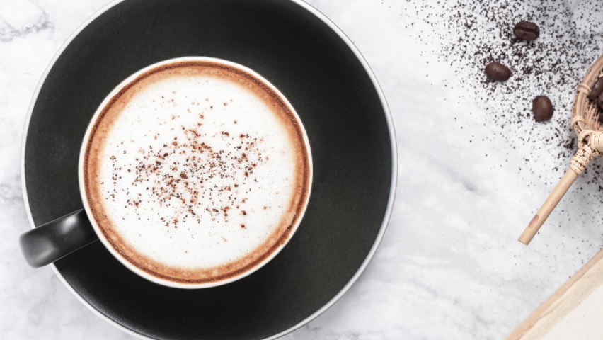Hot Cappuccino coffee with coffee beans the ground on marble table background. Coffee break at retro style coffee shop, top view for the menu.