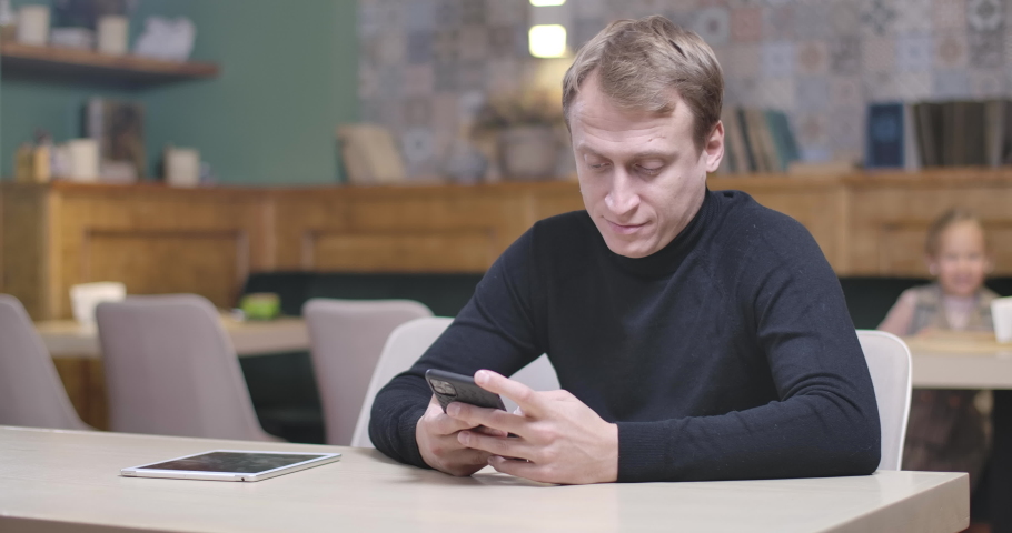 Concentrated man using smartphone sitting in restaurant as cute cheerful girl coming, taking device, and leaving. Daughter distracting father from social media on dinner. Cinema 4k ProRes HQ.