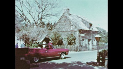 1970s: Car drives down street. Car with flat tire drives down street. Tire spins on top of display stand. Car drives through park. Car drives up to log cabin, people outside cabin wave.