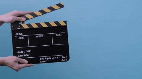 Movie Clapperboard. Film crew man hold and move up film slate in to the frame and clap it and move down out of the frame. yellow and black stripe clapperboard isolated blue background Video production