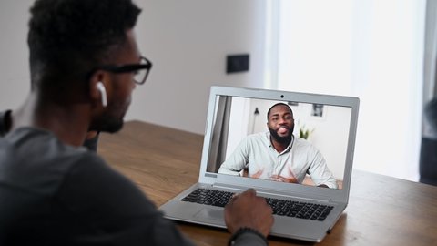 Back view African-American men talking online via video call, multiracial employees have video meeting. Two biracial guys using laptop for virtual conversation