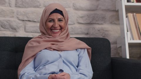 Beautiful face portrait of happy mature middle-aged woman in turban. Elderly woman in turban, healthy cheerful smiling, looking at camera posing at home, looking for portrait.Slow motion video.