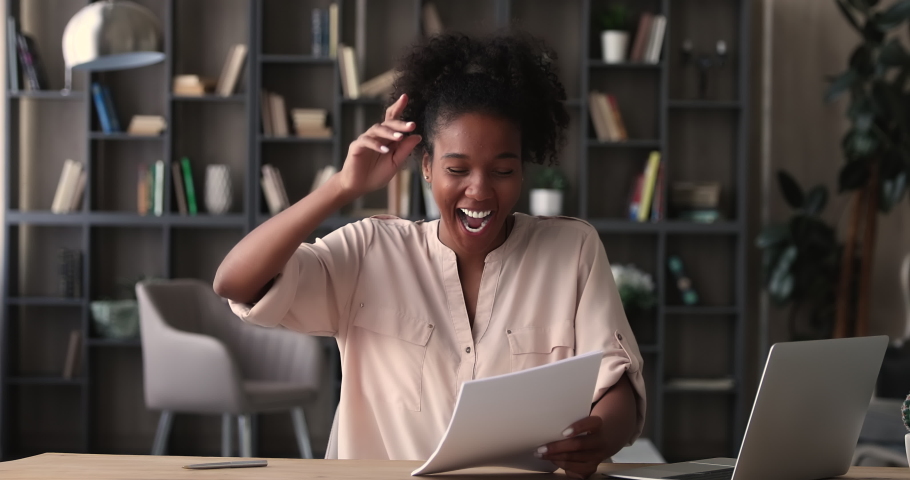 Happy young african woman sit at table holding documents sheets, read good news in paper letter feels overjoyed. Profit notification from bank, deal confirmation, financial statement, success concept | Shutterstock HD Video #1065219289