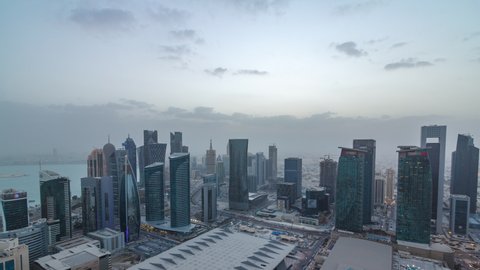 Skyline of the West Bay area from top in Doha day to night transition timelapse, Qatar. Illuminated modern skyscrapers aerial view from rooftop at evening after sunset. Traffic on the road