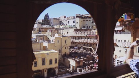 FEZ, MOROCCO - OCTOBER 2020: Elevated Slow Motion Crane Wide Shot Through Balcony Window To People Working In The Chouara Tannery Below, Tanning Leather From Large Pots Of Dye, Fez, Morocco