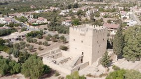 A large old, historic castle with towers stands in a landscaped location with tree houses and fields. Aerial view Cyprus.