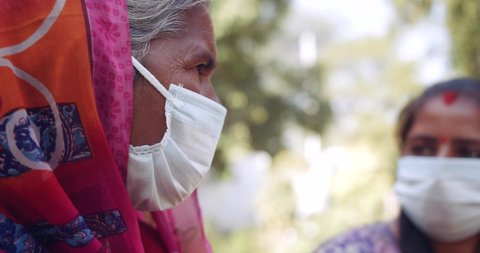 Slow-motion handheld of one senior aged old lady and a young woman with surgical protective face mask, wearing colorful pink Sari, togetherness outdoors talk discuss chat share