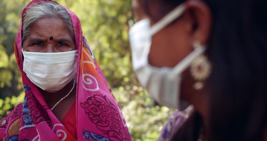 Slow-motion handheld of one senior aged old lady and a young woman with surgical protective face mask, wearing colorful pink Sari, togetherness outdoors talk discuss chat share