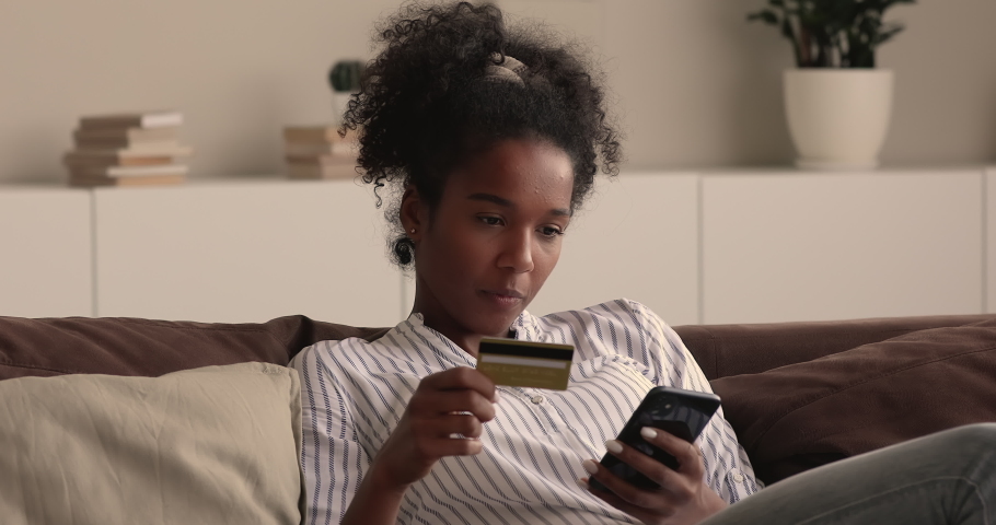 Young african woman rest on couch hold smartphone and credit card enjoy easy instant money transfer, makes good deed on-line donation secure payment. Happy customer and online retail services concept Royalty-Free Stock Footage #1065237316