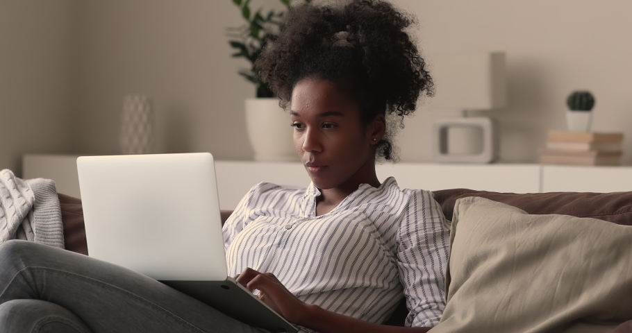 Young african woman sit on couch read great unbelievable fantastic news on laptop feels happy celebrate success in online lottery, betting auction. Student get scholarship or female got hired concept Royalty-Free Stock Footage #1065237649