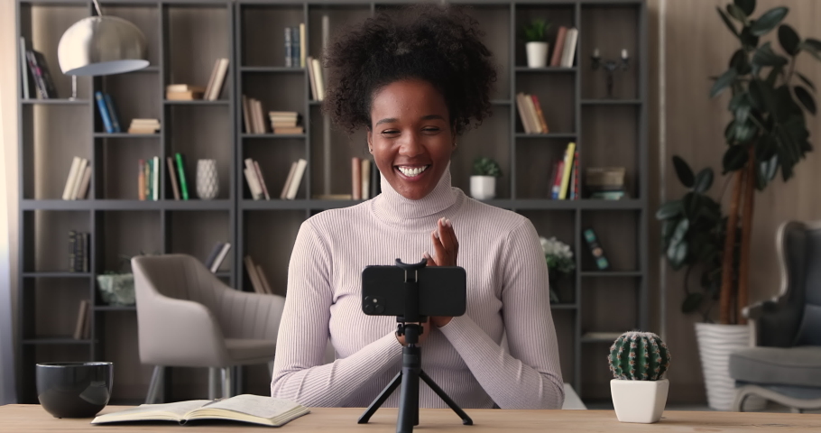 Happy young african woman vlogger sit at desk indoor put device on tripod record on smartphone new vlog, share information, experience, knowledge. Webinar, video call event, streaming activity concept Royalty-Free Stock Footage #1065237790