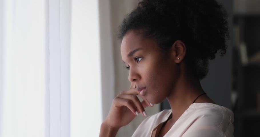 Young african woman standing indoor looking out window thinking, lost in sad thoughts having personal life or health concerns feels upset. Break up, divorce, psychological disorder, loneliness concept | Shutterstock HD Video #1065237835