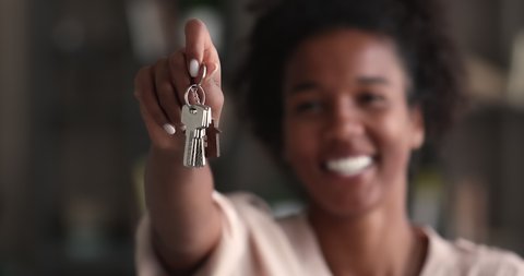 Mixed-race woman holding keys, close up focus on hand. Realtor real estate agent selling property, make special offer of affordable dwelling, relocation day, happy homeowner person, bank loan concept