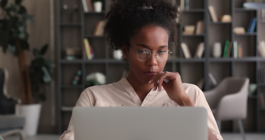 Pensive serious young african woman wear glasses lost in thoughts, working on online project, pondering strategy, searching solution and creative ideas, thinking over task sitting at desk with laptop Royalty-Free Stock Footage #1065238126